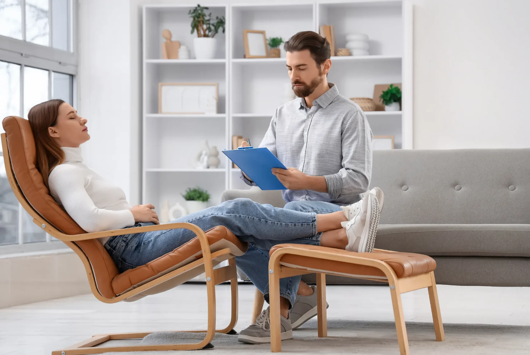 A therapist sitting beside a reclining client during a calm, guided relaxation session in a bright consulting room