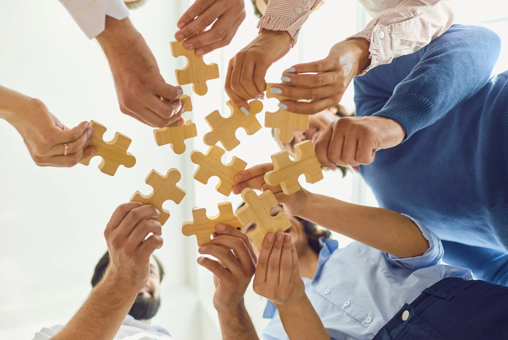 Several pairs of hands holding wooden puzzle pieces together, illustrating how separate experiences may connect into a pattern