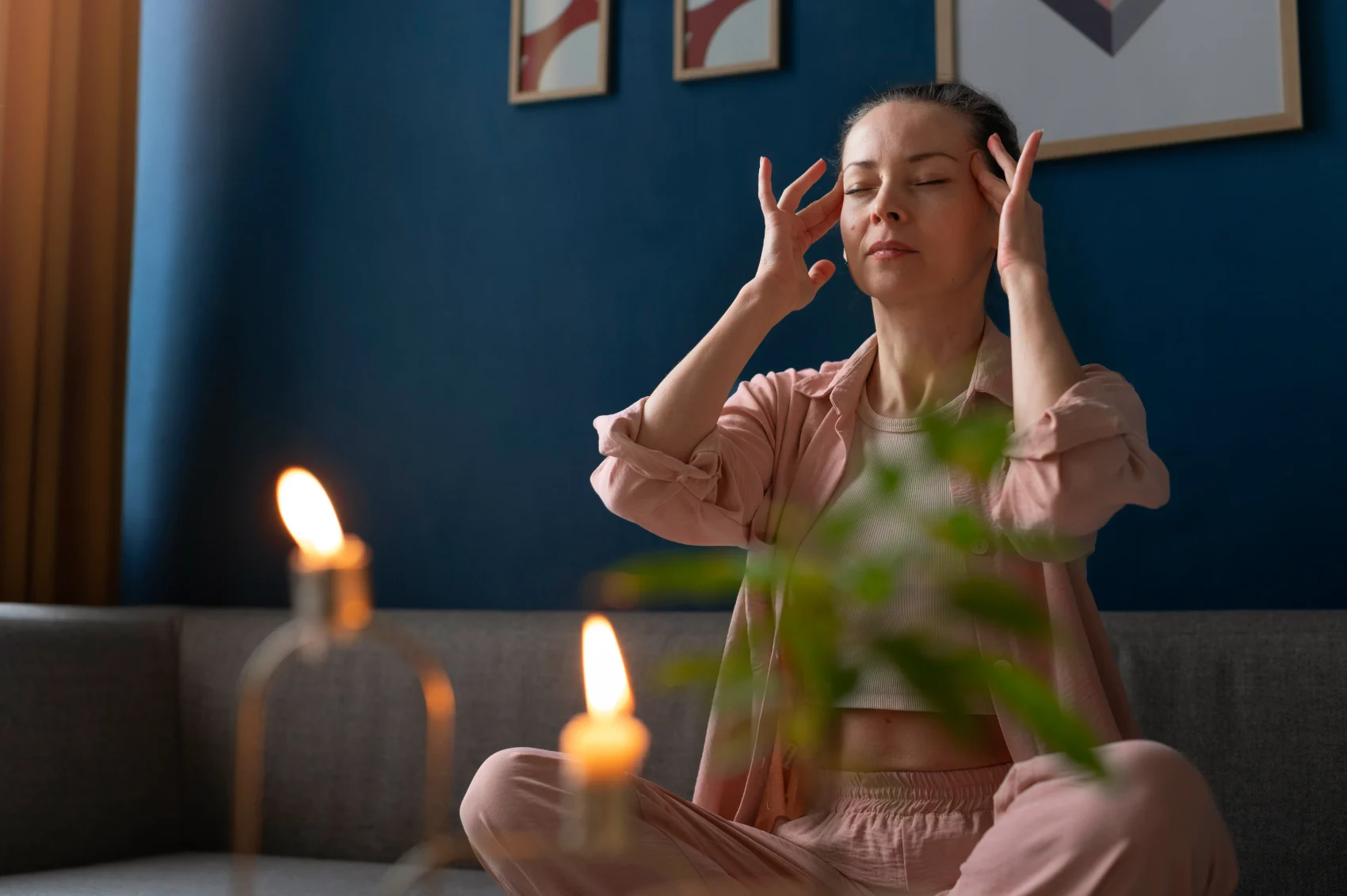 A person sitting quietly with eyes closed and fingertips at the temples, reflecting inwardly in a calm candlelit room