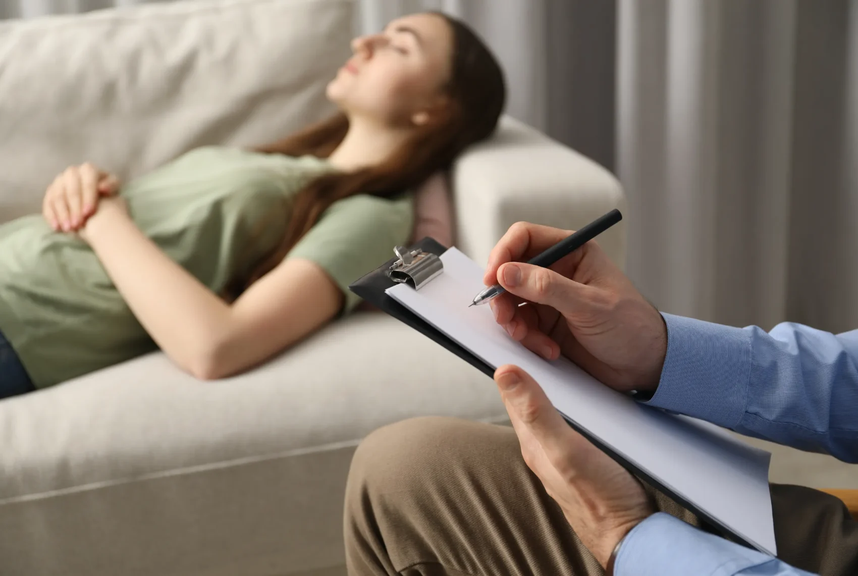 A practitioner making reflective notes on a clipboard while a client rests after a session